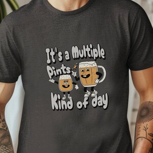 May include: A dark gray t-shirt with a humorous graphic of two cartoon beer mugs. The text on the shirt reads "It's a Multiple Pints Kind of Day."