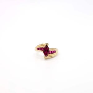 Op de afbeelding: Een gouden ring met een marquise-vormige robijn en kleinere robijn accenten. De ring heeft een delicaat, gebogen ontwerp.