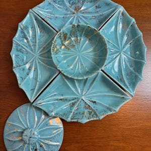 May include: A turquoise ceramic serving set consisting of four fan-shaped outer dishes, a central circular bowl, and a separate circular lid with a central knob. Each piece features a radial ribbed pattern and a distressed gold-tone finish.