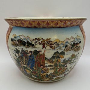 May include: A round ceramic planter featuring a hand-painted landscape scene with multiple figures in traditional attire. The rim is decorated with a repeating floral pattern in red and gold. The body displays mountains, trees, and water.