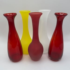 Könnte beinhalten: Eine Sammlung von fünf Glasvasen mit ausgestellten Rändern. Zwei sind glänzend rot, eine ist mattrot, eine ist leuchtend gelb und eine ist durchscheinend weiß. Die Vasen haben schlanke Hälse und abgerundete Körper, gruppiert auf einer Fläche.