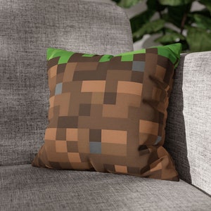 Może przedstawiać: Poduszka w kolorze brązowym i zielonym z pikselowym wzorem przypominającym blok ziemi z gry komputerowej Minecraft.