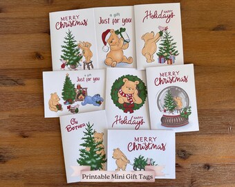 May include: A collection of Christmas-themed greeting cards featuring illustrations of a bear character. The cards have text that reads "Merry Christmas", "Happy Holidays", and "a gift Just for you". The cards are on a wooden surface.