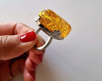 May include: A silver ring with a large, rectangular, yellow gemstone. The gemstone has a sparkly, textured surface.