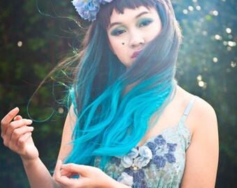 May include: A woman with teal blue hair wearing a blue and white flower crown and a light blue lace dress.