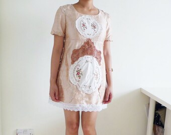 Puede incluir: Un vestido beige con detalles de encaje y un ribete de encaje blanco. El vestido está hecho de una tela ligera y tiene un corte holgado. La modelo lleva sandalias de tacón naranja.