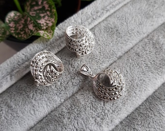 May include: A set of silver earrings and a pendant necklace with a swirling design, all encrusted with sparkling marcasite stones.