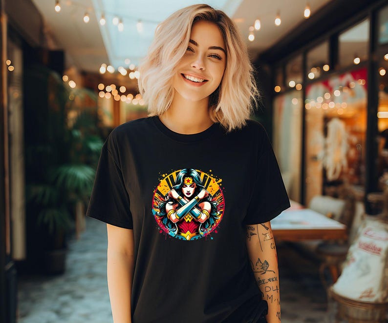 May include: Black t-shirt with a colorful graphic of Wonder Woman with her arms crossed. The graphic is surrounded by a yellow and orange splattered paint effect.