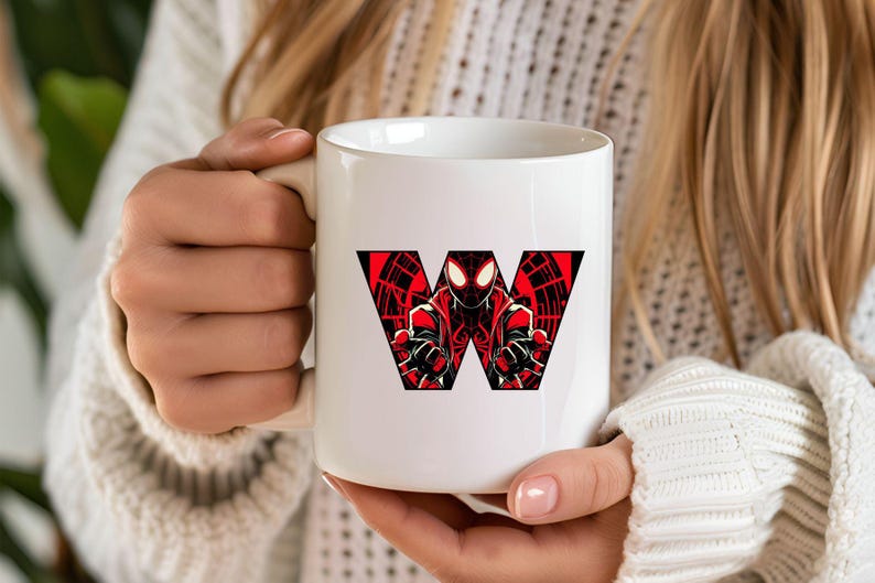 Może przedstawiać: Biały kubek ceramiczny z czerwoną i czarną grafiką postaci superbohatera tworzącego literę "W".
