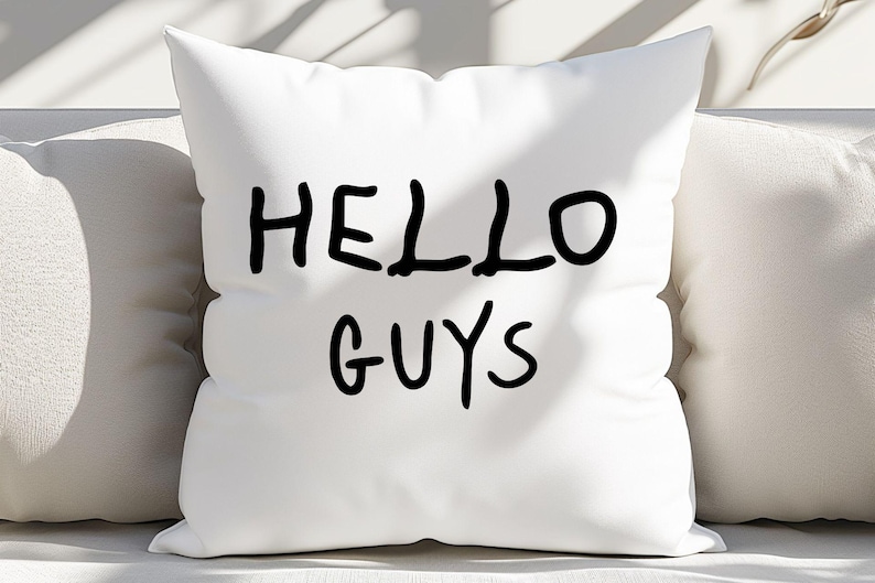 K&ouml;nnte beinhalten: Ein wei&szlig;es Kissen mit schwarzem handgeschriebenem Text, der "HELLO GUYS" auf wei&szlig;em Hintergrund lautet.