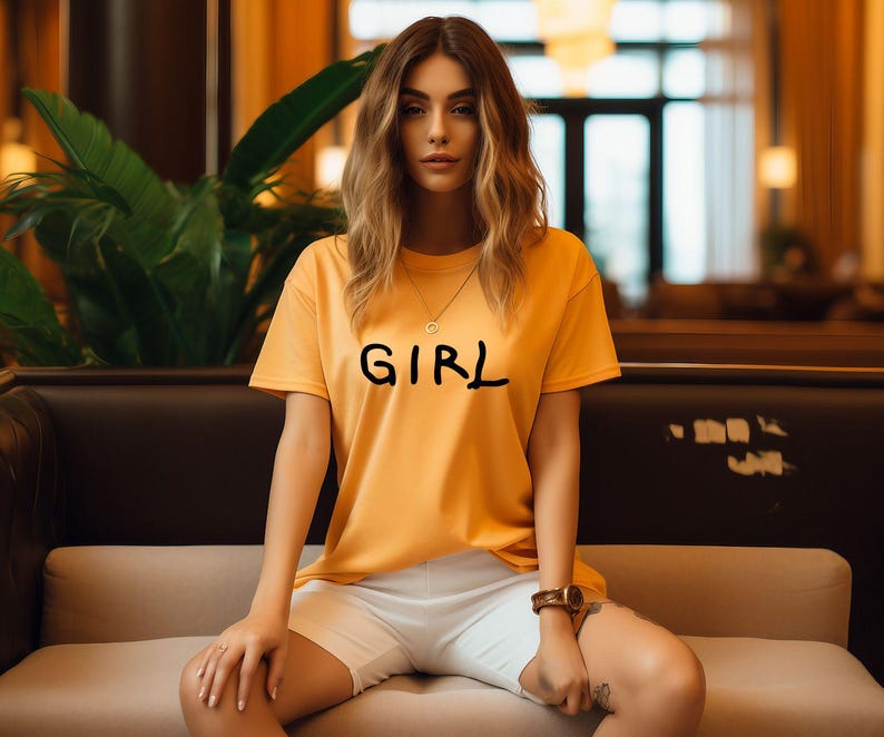 K&ouml;nnte beinhalten: Eine Frau tr&auml;gt ein gelbes T-Shirt mit dem Aufdruck "GIRL". Sie sitzt auf einem Sofa und tr&auml;gt wei&szlig;e Shorts.