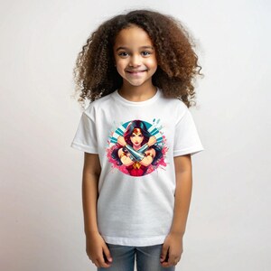 May include: White t-shirt with a colorful graphic of Wonder Woman with her arms crossed. The graphic is surrounded by a blue and white circle with pink and blue splatters.