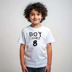 K&ouml;nnte beinhalten: Wei&szlig;es T-Shirt mit schwarzem Text, auf dem "BOY STORY 8" steht. Ein Kind tr&auml;gt das Shirt.