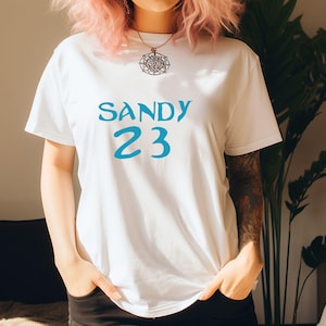 May include: White t-shirt with blue text that says "SANDY 23".