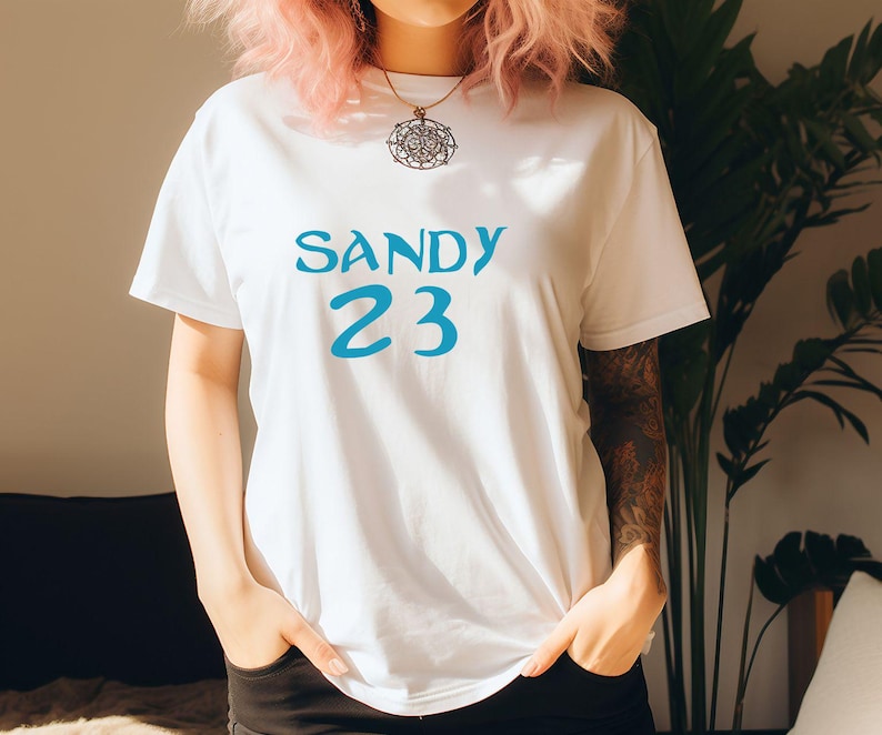 May include: White t-shirt with blue text that says "SANDY 23".