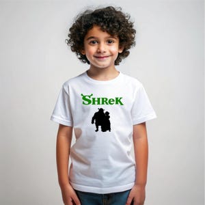 Pu&ograve; includere: Maglietta bianca con un logo verde "Shrek" e una silhouette nera di Shrek e Fiona.