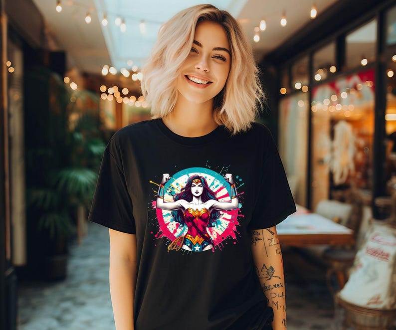 May include: Black t-shirt featuring a colorful graphic of Wonder Woman. The design includes a portrait of the superheroine within a blue and pink circular splash. The shirt is a classic crew neck style.