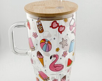 Op de afbeelding: Een doorzichtige glazen beker met een handvat, bamboe deksel en rietje. De beker is versierd met kleurrijke illustraties met een zomerthema, waaronder een flamingo, ijsjes en zonnebrillen. De beker is ontworpen voor koude dranken.