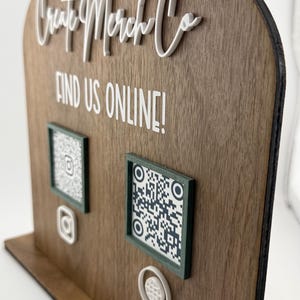 Könnte beinhalten: Holzdisplay mit dem Text "Create Merch Co" und "FIND US ONLINE!". Es verfügt über zwei QR-Codes und Instagram-Symbole. Das Display hat eine dunkle Holzmaserung und eine abgerundete Oberseite.