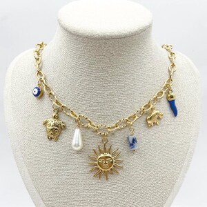 May include: Gold chain necklace with multiple charms, including a sun, a turtle, an elephant, a pearl, a blue evil eye, and a blue and white ceramic charm.