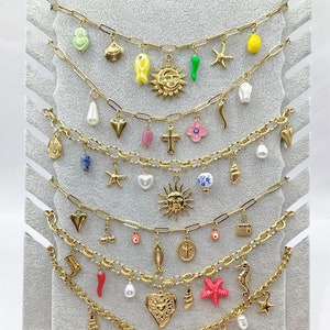 Peut inclure: Un ensemble de six colliers en chaîne dorée avec divers pendentifs, notamment des cœurs, des étoiles, des coquillages, des poissons, des croix, des soleils et d'autres éléments décoratifs. Les pendentifs sont en émail et en verre colorés.