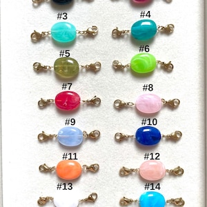 Peut inclure: Seize perles de forme ovale de différentes couleurs, chacune dotée de fermoirs mousquetons en métal doré aux deux extrémités. Les perles sont numérotées de #1 à #16 et présentent des finitions marbrées ou unies dans des tons de bleu, rose, vert, rouge, orange, blanc et beige.
