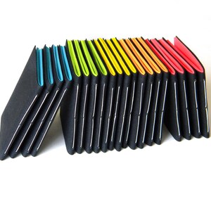 May include: A series of black, accordion-style notebooks with colorful edges. The edges transition from blue to green, yellow, orange, and red. Each notebook is held together with white stitching.