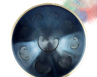 May include: A steel tongue drum with a dark blue finish and a gold-colored rim. The drum features etched designs and the text "Rav Vast Since 2013". The instrument is designed for musical performance.