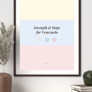 Puede incluir: Una lámina de arte mural enmarcada con tres bloques de color horizontales en amarillo pálido, azul claro y rosa suave. El texto "Strength & Hope for Venezuela" está centrado en negro, seguido de tres pequeños corazones delineados en amarillo, azul y rojo.