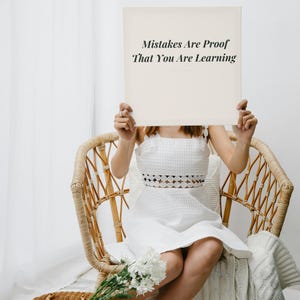 Puede incluir: Un vestido blanco sin mangas de tela texturizada con un detalle de corte circular en la cintura. El vestido se combina con un letrero cuadrado con el texto impreso en negro: Mistakes Are Proof That You Are Learning. La prenda tiene un escote cuadrado.
