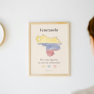 Puede incluir: Una lámina enmarcada con un mapa en acuarela de Venezuela en amarillo, azul y rojo. El texto dice Venezuela, Por cada lágrima, un acto de solidaridad, con tres corazones pequeños en amarillo, azul y rojo debajo.