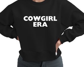 May include: Black crew neck sweatshirt with the white text "COWGIRL ERA". The sweatshirt has a ribbed hem and cuffs. The model is wearing blue jeans.