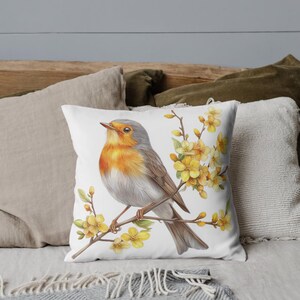May include: White square throw pillow featuring a watercolor illustration of a robin perched on a branch with yellow flowers. The bird has orange, gray, and brown feathers. The pillow is on a bed with other pillows.