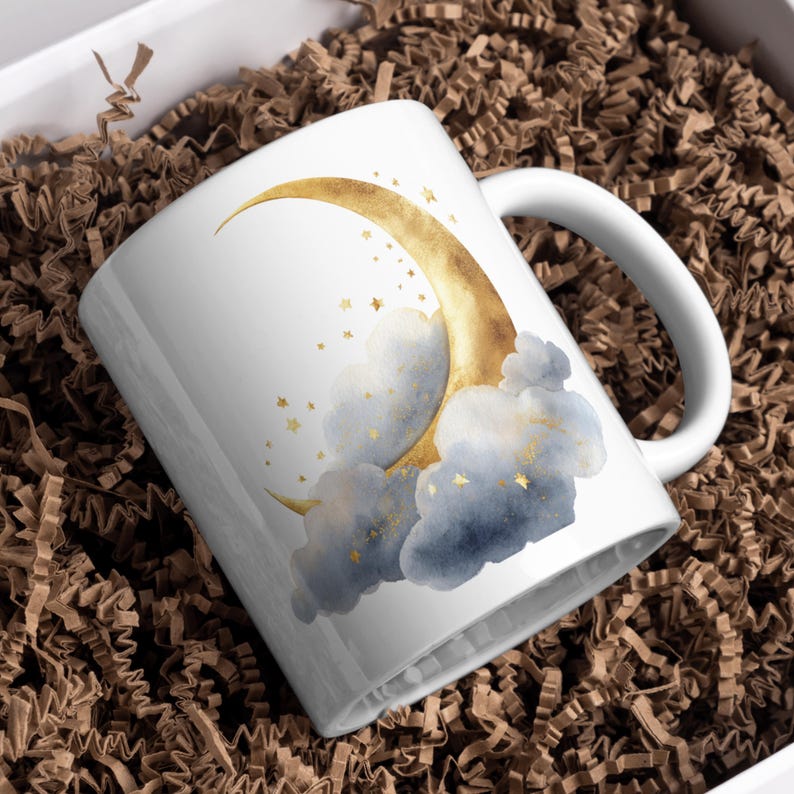 Puede incluir: Taza de cer&aacute;mica blanca con una luna creciente dorada, estrellas doradas y nubes azules de acuarela. La taza tiene un asa blanca y se presenta en una caja blanca con relleno de papel marr&oacute;n. Tema celestial.