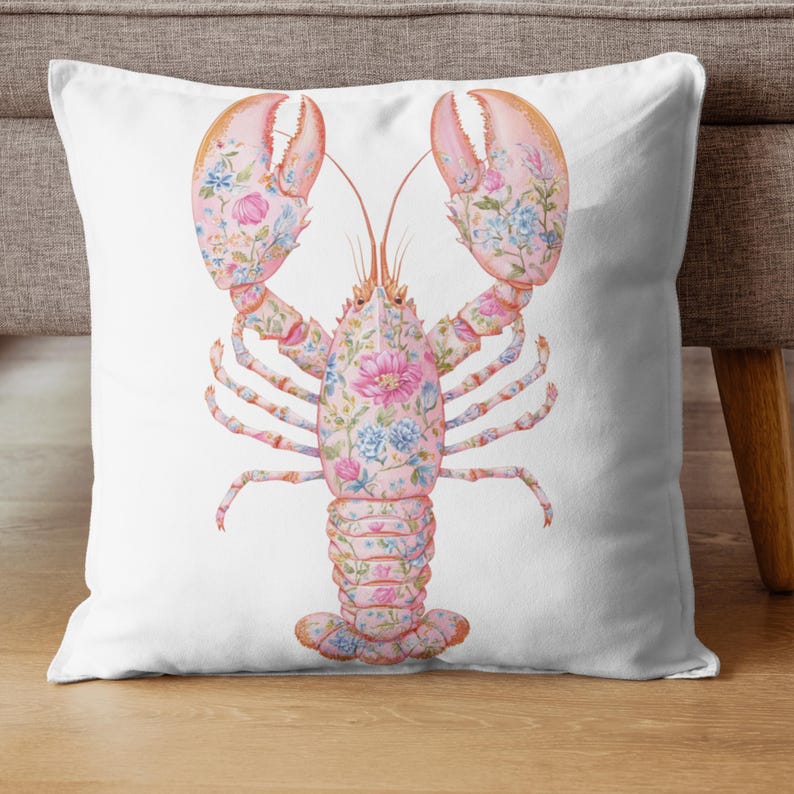 May include: A square throw pillow featuring a white background with a central illustration of a lobster. The lobster is light pink and decorated with a detailed pattern of blue, pink, and white flowers and green leaves across its entire body.