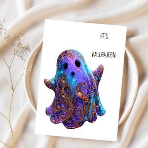 Op de afbeelding: Een Halloween-wenskaart met een gestileerd spook met ingewikkelde paarse, blauwe en gouden patronen. De kaart leest "IT'S HALLOWEEN" in zwarte tekst. De kaart staat tegen een witte achtergrond.