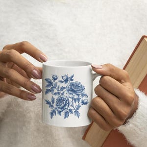 May include: White ceramic mug featuring a blue floral design. The design includes detailed illustrations of peonies and leaves. The mug has a standard handle and a smooth, glossy finish. A classic and elegant design for everyday use.