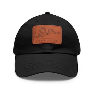 Puede incluir: Una gorra de béisbol negra con un parche de cuero marrón que presenta una serpiente enroscada y el texto "JOIN, or DIE."