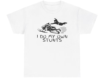 Puede incluir: Camiseta blanca con un gráfico negro de una persona haciendo una acrobacia en moto de nieve. El texto "I do my own stunts" está impreso debajo del gráfico.