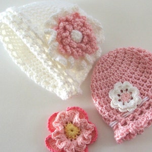 Peut inclure: Deux chapeaux en crochet avec des fleurs roses et blanches. Un chapeau est blanc et l'autre est rose.