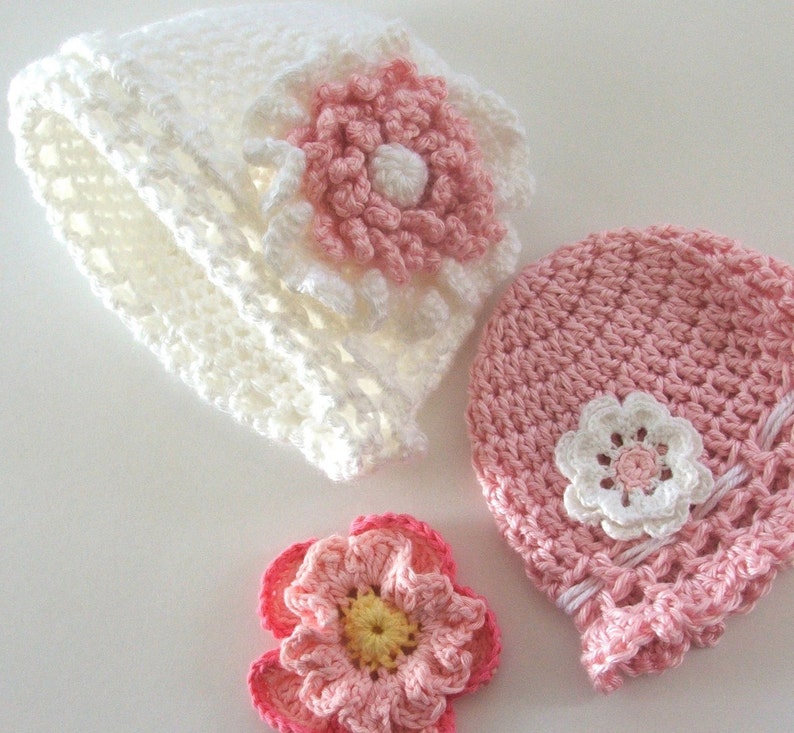 Peut inclure: Deux chapeaux en crochet avec des fleurs roses et blanches. Un chapeau est blanc et l'autre est rose.