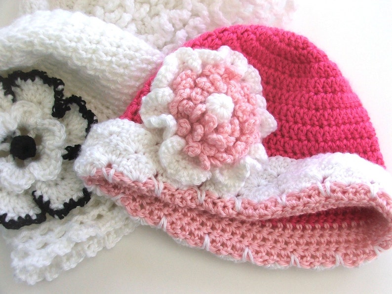 Peut inclure: Un chapeau crochet&eacute; rose et blanc avec une grande fleur blanche sur le dessus. Le chapeau est fait avec une vari&eacute;t&eacute; de points et a une bordure rose et blanche.