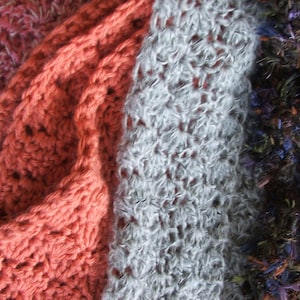 May include: A close-up of a multi-colored knitted scarf with different textures. The scarf is made of a soft, fuzzy yarn and has a variety of colors, including pink, red, white, brown, and blue.