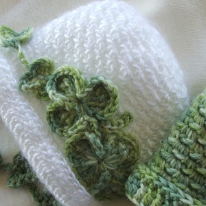 May include: White crocheted hat with a green clover design. The hat is made with a soft, textured yarn.