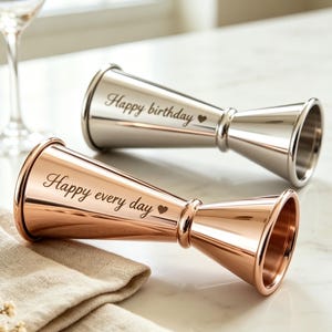 May include: Two double-sided metal jiggers, one in a polished silver finish and one in a rose gold finish. Each jigger features an engraved inscription: the silver one reads Happy birthday with a heart, and the rose gold one reads Happy every day with a heart.