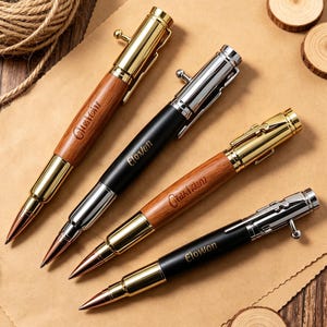 May include: Four bolt-action pens arranged diagonally. Two pens feature wood barrels with gold-tone hardware, while two feature matte black barrels with silver-tone hardware. Each pen has a pointed tip and a bolt-action mechanism on the cap.