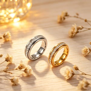 May include: Two rings, one silver and one gold, are displayed on a wooden surface. Both rings feature a band of clear stones. The silver ring has the inscription "In My Heart". The gold ring has the inscription "P & B".