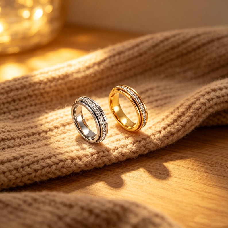 May include: Two rings, one silver and one gold, each adorned with a row of sparkling gemstones. The rings are set against a textured, tan fabric, with soft lighting creating a warm ambiance. The rings are a classic jewelry item.