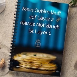 Könnte beinhalten: Spiralgebundenes Notizbuch mit blauem Einband. Auf dem Einband steht der Text "Mein Gehirn läuft auf Layer 2 dieses Notizbuch ist Layer 1", sowie eine Kette und ein Schloss. Am unteren Rand des Notizbuchs ist ein Stapel Goldmünzen zu sehen.