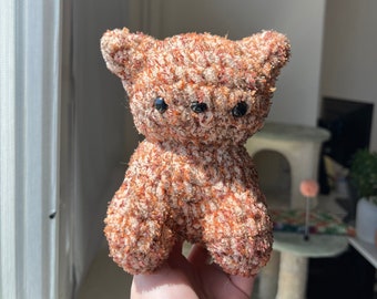 Könnte beinhalten: Ein kleiner, brauner und weißer Teddybär mit schwarzen Augen. Der Bär ist aus weichem, flauschigem Material.